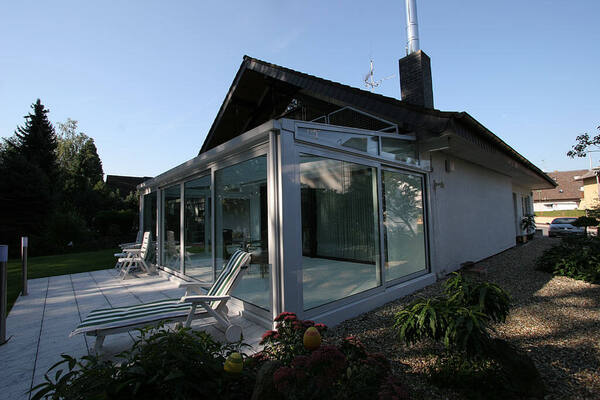 Modernes Einfamilienhaus mit Wintergarten und Terrasse im Grünen bei Sonnenschein.