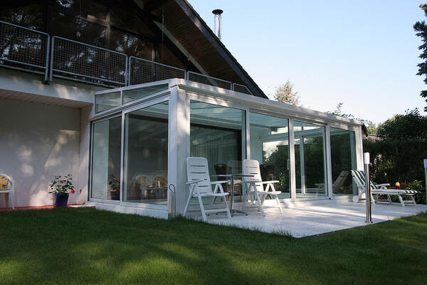 Moderner Wintergarten mit Glasfront und Gartenmöbeln auf sonniger Terrasse am Haus.