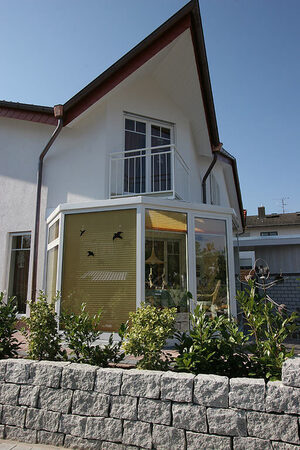 Modernes Einfamilienhaus mit Wintergarten, weißen Wänden und gepflegtem Garten.