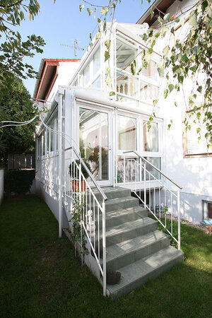 Moderner Wintergarten mit Glasfassade und Treppe an Einfamilienhaus im Grünen.