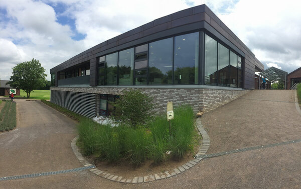 Modernes Gebäude mit großen Glasfronten, umgeben von Grünflächen und Zufahrtswegen.