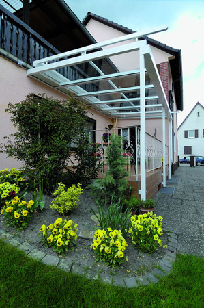 Überdachte Terrasse mit Glasdach an Einfamilienhaus, umgeben von Blumenbeet und Garten.