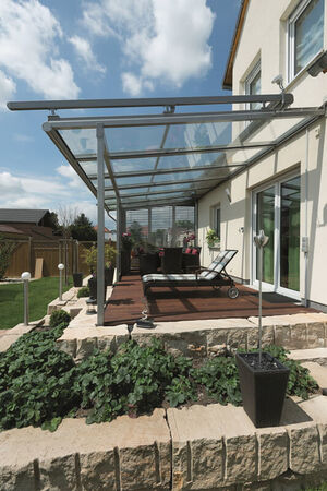 Moderne Terrasse mit Glasdach am Einfamilienhaus, Holzboden und Gartenbepflanzung.